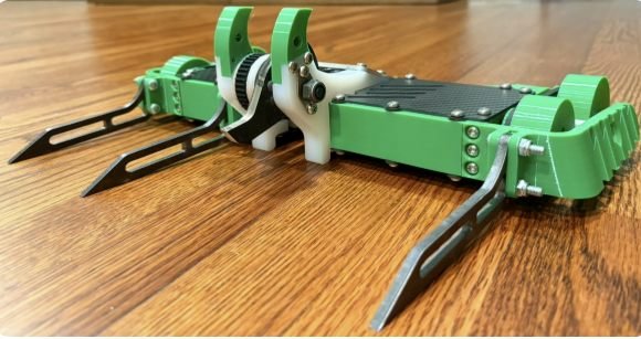 The finished robot on a wooden floor, low front view showing the steel tines and green uprights.
